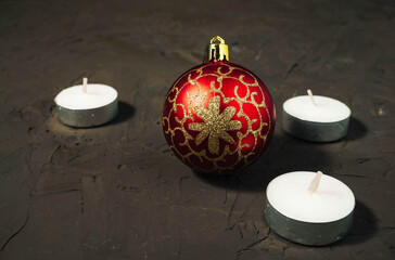 Decorative Christmas tree ball in red and gold color and flat candles on a dark background