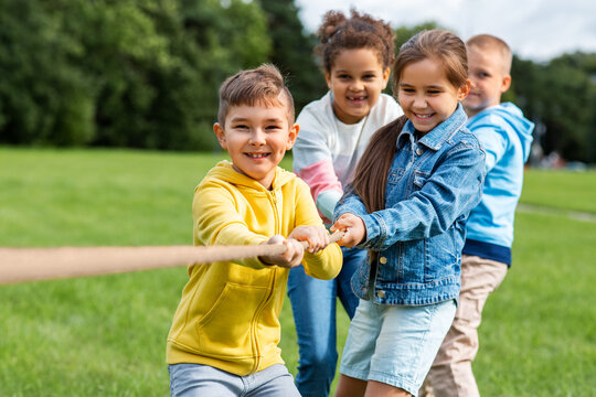 childhood, leisure and people concept - group of happy kids playing tug-of-war game and running at park
