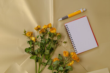 Faded flowers and a blank open notebook with a pen against a cre