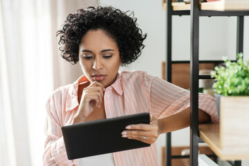 home improvement, technology and people concept - woman with tablet pc computer standing at shelf and thinking