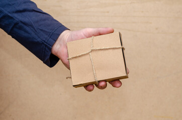 An adult male is holding a brown gift box in his hand. The recta