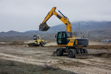 yellow excavator works against the background of mountains.