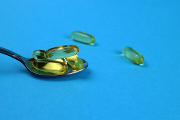 Omega 3 capsules, fish oil in a spoon on a blue background