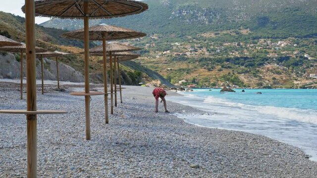 Agia Kiriaki Beach, Zola In Kefalonia, Greece - A Tourist Man Picking Up Pebbles And Throwing Them Into The Sea. - Wide Shot