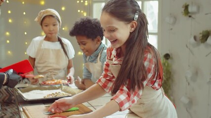 Happy little girl taking freshly baked pizza from chef, enjoying small and smiling during cooking lesson in kitchen