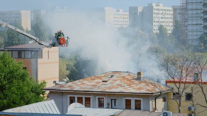 Close up of firefighters on platform truck helping with fire from burning building. Firemen with...