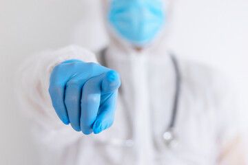 young male doctor in protective suit and blue protective gloves and mask with stethoscope shows his index finger and asks if you have been vaccinated