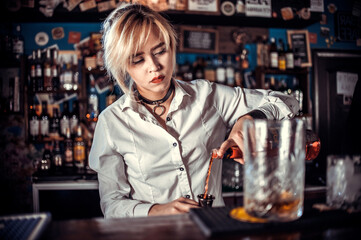 Focused woman bartending makes a cocktail at the bar counter