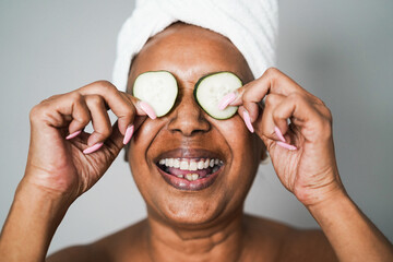 Senior african woman having fun holding cucumber skin care therapy - Focus on vegetables