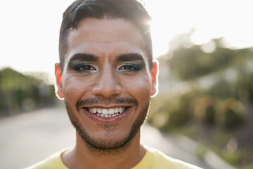 Young transgender man with makeup smiling on camera at pride event - Focus on face - obrazy, fototapety, plakaty