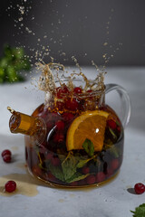 Tea splash with citrus, cranberries and mint in a glass teapot. Splashing tea. Healthy tea.