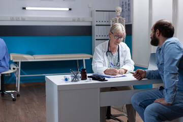 Obraz premium Woman doctor signing checkup files to give treatment to man after examination. Physician writing prescription medicine and signature on papers to help patient at medical appointment.