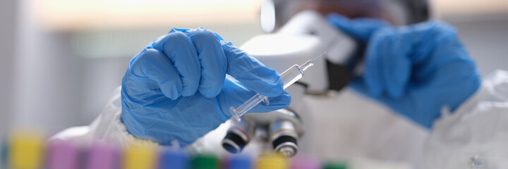 Scientist looks through microscope at glass syringe with needle