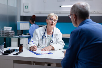 Obraz premium Specialist doing signature on checkup files to give prescription treatment to ill man. Woman doctor signing documents after healthcare consultation, giving medicine to old patient.