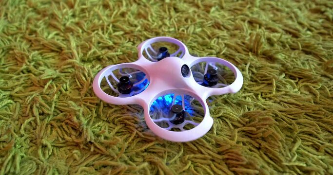 small indoor home brushless fpv quadcopter lies on carpet and is ready to fly and shines with neon colorful lights 
