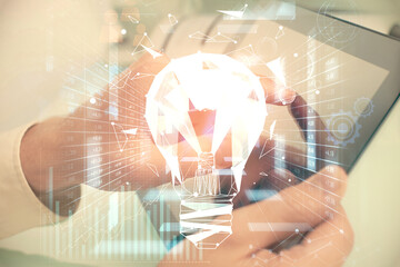 Double exposure of man's hands holding and using a digital device and bulb hologram drawing. Idea concept.