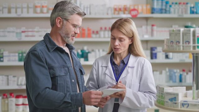 Customer male adult wearing glasses reading medical prescription for prescribed medicine drugs from pharmacist doctor. Drugstore. Medical sector.