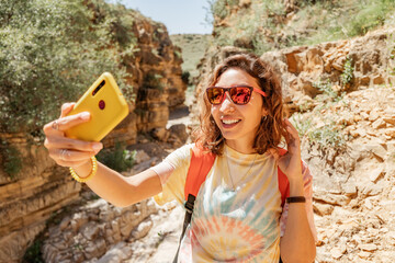 A female travel blogger takes selfies for her social networks in a picturesque canyon in the desert - obrazy, fototapety, plakaty