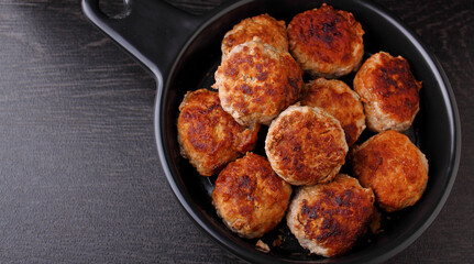 Meat cutlets decorated with basil in a black frying pan on a black background. Top view.