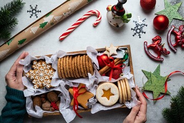 Gift wooden box with tasty homemade cookies and nuts in hand on gray background. Christmas and New Year concept. Snowflake gingerbread, austrian linzer cookies. Top view, holidays flat lay.