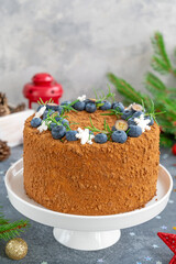 Chocolate honey cake decorated with fresh blueberries, rosemary and sugar snowflakes on top of a white stand. Cake for Christmas and New Year. selective focus