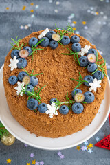 Chocolate honey cake decorated with fresh blueberries, rosemary and sugar snowflakes on top of a white stand. Cake for Christmas and New Year. selective focus