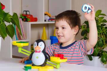 A preschool boy learns numbers, weighs numbers on a penguin scale