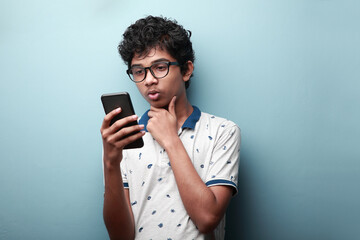 Young boy of Indian origin looking at his mobile phone with a doubtful face expression