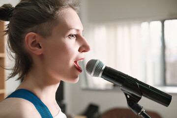 young emotional woman singing into a microphone. female rock singer on a rehearsal in record studio. side view