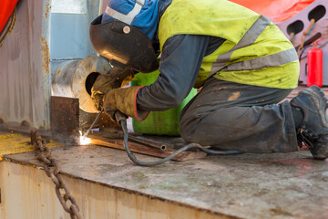 Deck crew performing welding of lashing stoppers for safe cargo securing.