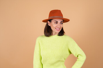 Fashionable stylish woman in full growth on a beige background in trousers, a sweater and a hat looks to the side, smiling