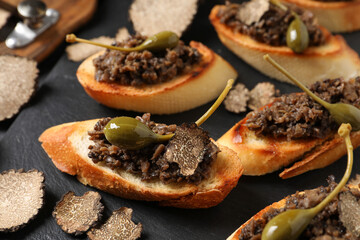 Tasty bruschettas with truffle paste and capers on black table, closeup