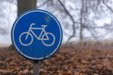 Dutch round blue bicycle sign depicting a bike in the middle of the woods with the autumn forest behind cloaked in early morning dew drop mist giving it an eery foggy atmosphere