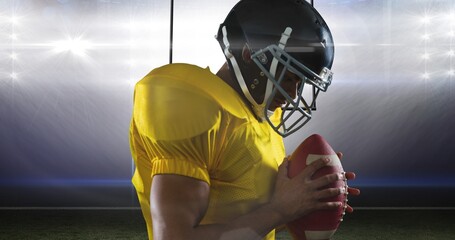 Fototapeta na wymiar Side view of male american football athlete wearing helmet and yellow jersey holding ball at stadium