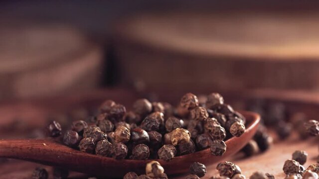 Black pepper falling on a wooden spoon.Slow motion. Close up