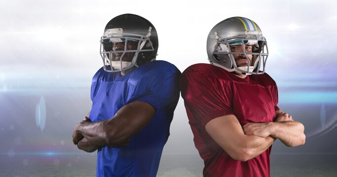 Portrait of rival american footballers standing back to back with arms crossed at stadium