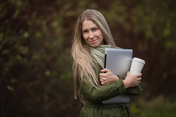 Beautiful girl looks at the camera with a laptop in the autumn park. Space for text and space for copy. Remote work, distance learning. Online shopping and social media concept