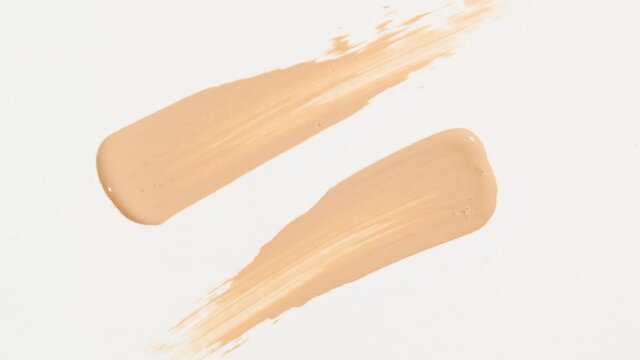 Macro shot and slow motion of a brush, applicator, smear, concealer isolated on white background. Advertising professional cosmetics. Closeup of a cosmetic liquid foundation or cream beige color. 4k 