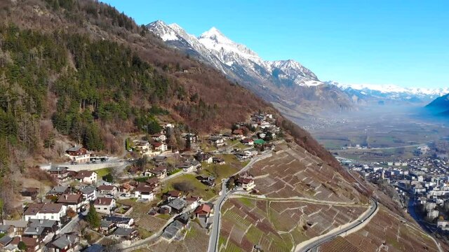 Aerial: vineyards in the Valais with a road and some cars passing nerby and snow covered mountains in the background