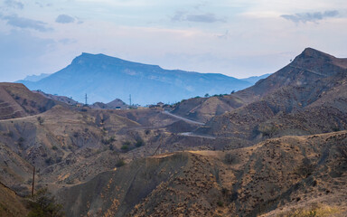 Panorama of the evening mountains with a complex landscape. Mountain serpentine in the dawn sunlight. Dangerous narrow dirt mountain road through the hills to a high-altitude village.