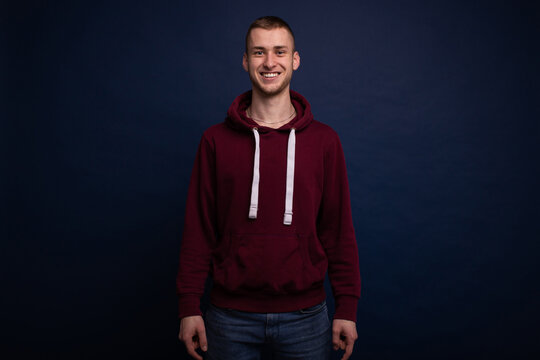 Smiling young man in red hoodie and jeans posing on blue background
