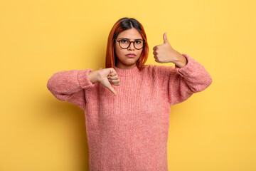 young hispanic woman feeling confused, clueless and unsure, weighting the good and bad in different...