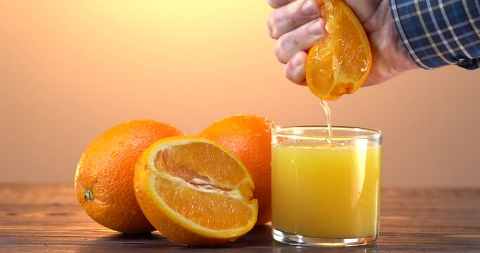 Man hand squeezes the juice out of the fresh orange. Many sliced oranges on the table. Glass with freshly squeezed drink. Helthy and care concept.