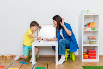 Woman speech therapist helps a boy correct the violation of his speech