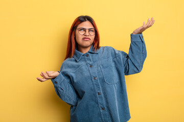 young hispanic woman shrugging with a dumb, crazy, confused, puzzled expression, feeling annoyed...