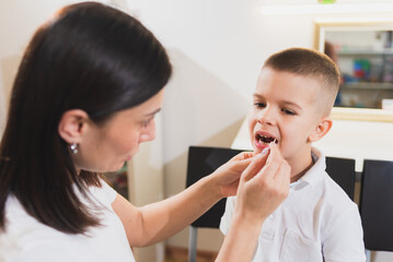 Woman speech therapist helps a child correct the violation of his speech in her office
