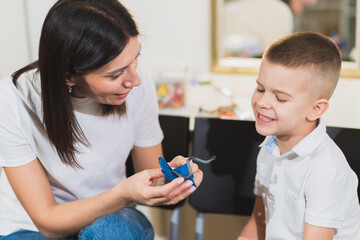 Woman speech therapist helps a child correct the violation of his speech in her office