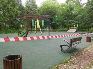 A beautiful playground with play complexes and a bench is fenced with a red and white ribbon. Restrictions during the pandemic, a ban on being in public places.