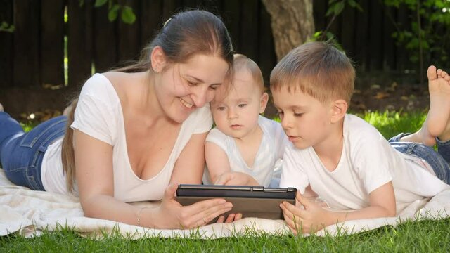 Happy mother with older and baby son browsing internet in park on tablet computer. Parenting, family, children development, and technology