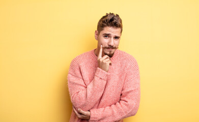 young handsome man looking happy and smiling with hand on chin, wondering or asking a question,...